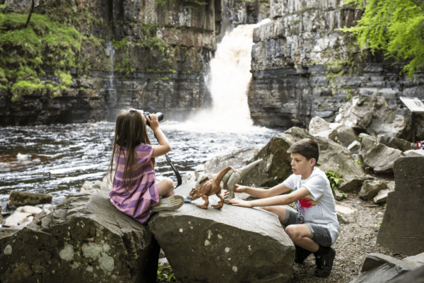 Kids playing with dinosaur toys in front of the waterfall