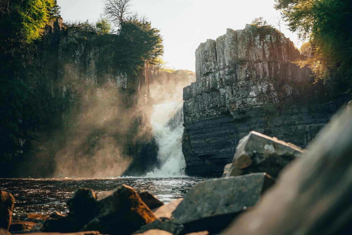 Photographer capturing High Force Waterfall at sunset, surrounded by glowing woodland.