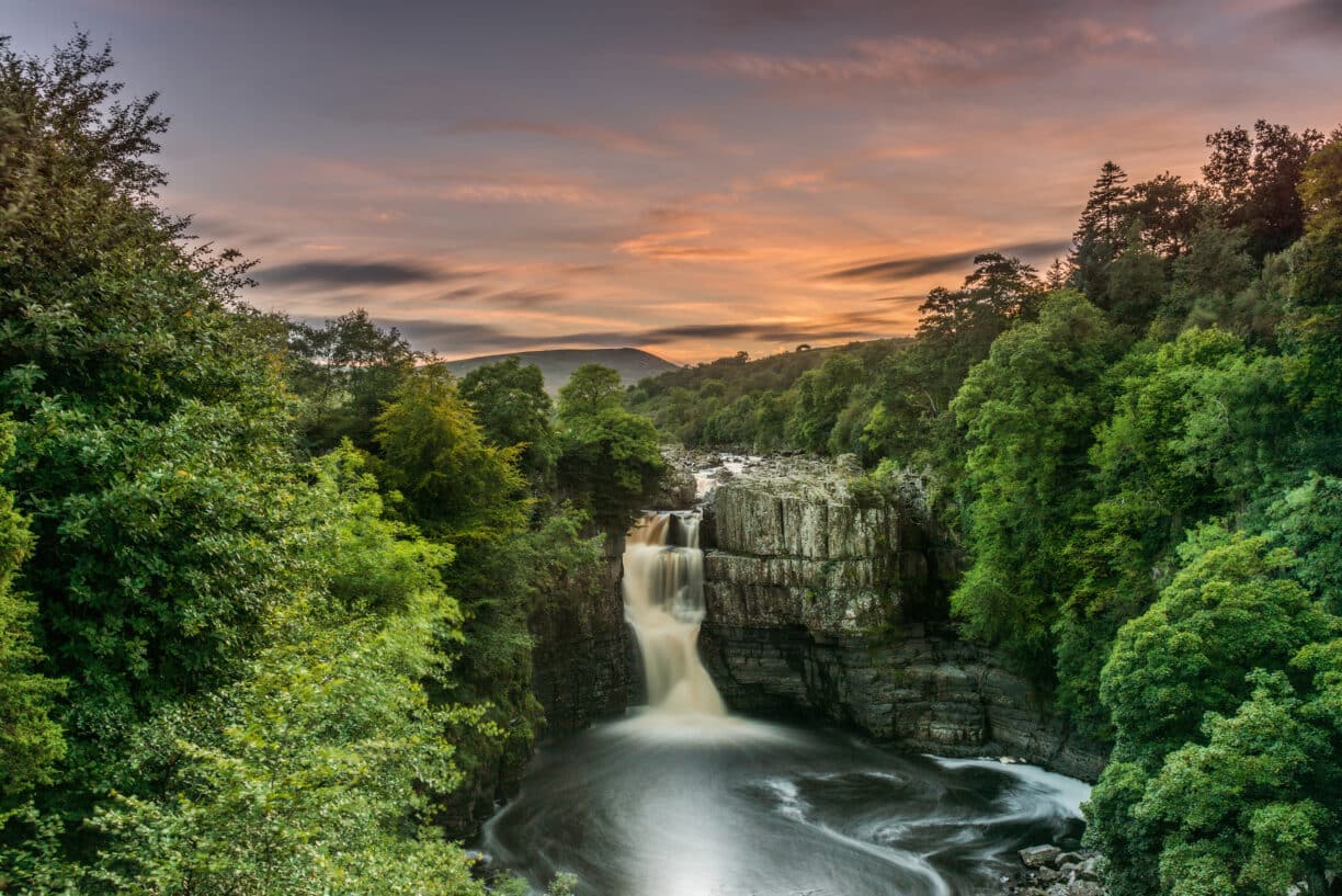 High Force Waterfall cascading powerfully over rocks during golden hour with warm sunset light.